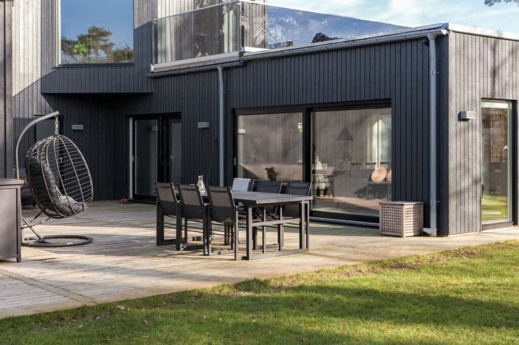 Uteplats med matbord, svart trähus i bakgrunden.